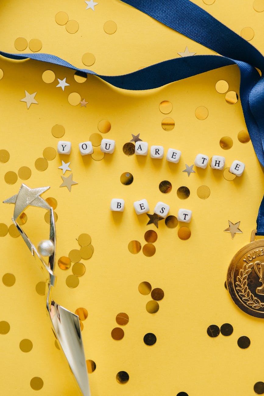 dice with you are the best message on yellow background beside medal on ribbon and statuette